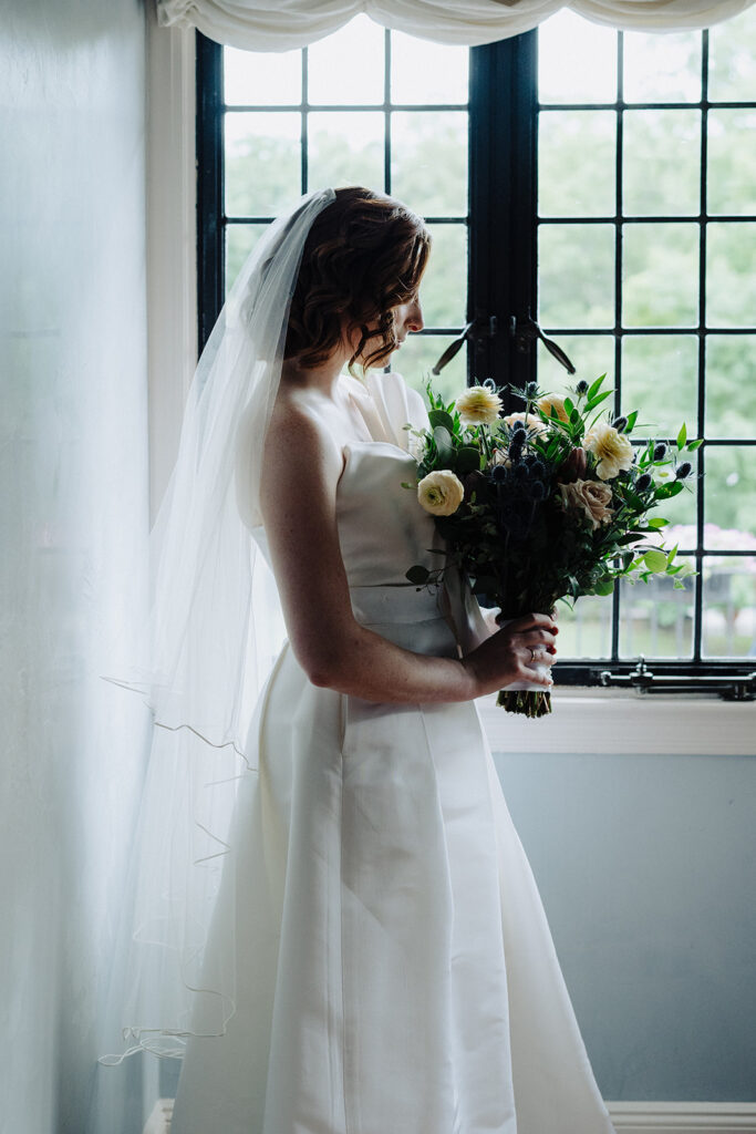Bride posing with her bouquet and in her elegant wedding dress in her Pleasantdale Chateau suite