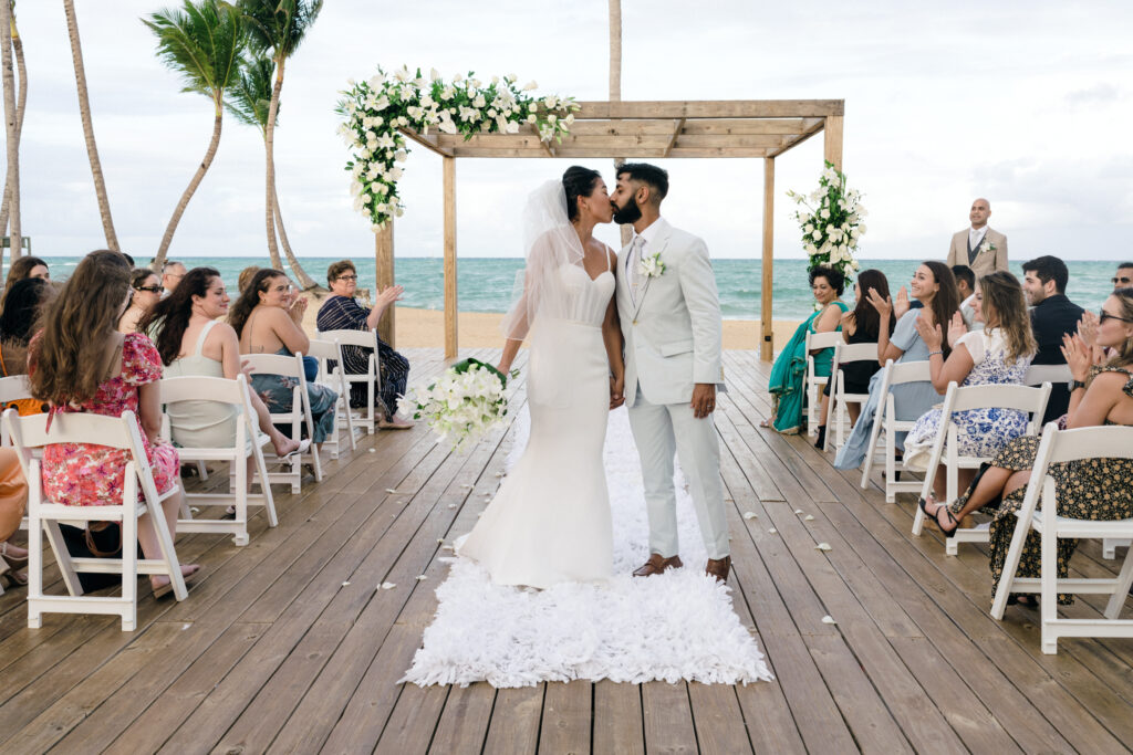Destination Wedding Photographer and Videographer (Hiring Checklist). Couple sharing a kiss in the middle of the aisle with their guests applauding.
