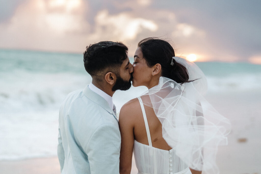 Bride and groom sharing a kiss with view of the ocean waves in front of them, captured by For Fearless Hearts