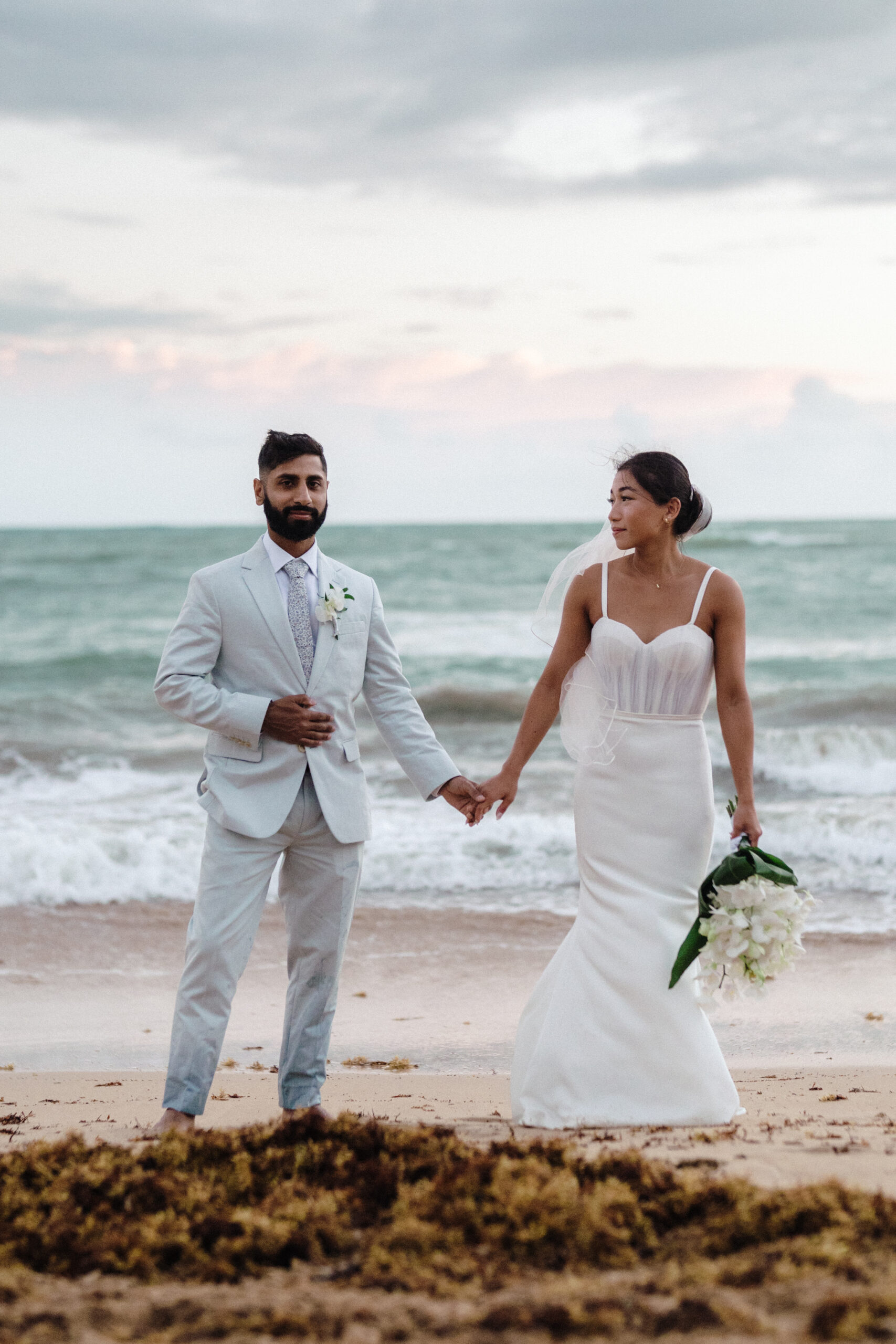 Bride and groom holding hands on the beach, captured by For Fearless Hearts
